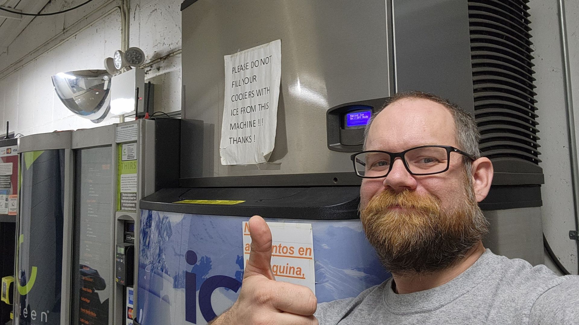 Man with glasses giving thumbs up by ice machine with warning sign